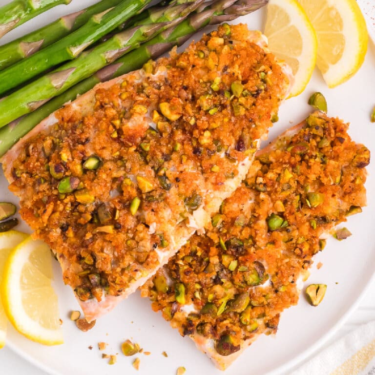 Pistachio crusted salmon on a plate with asparagus and lemon on a table.