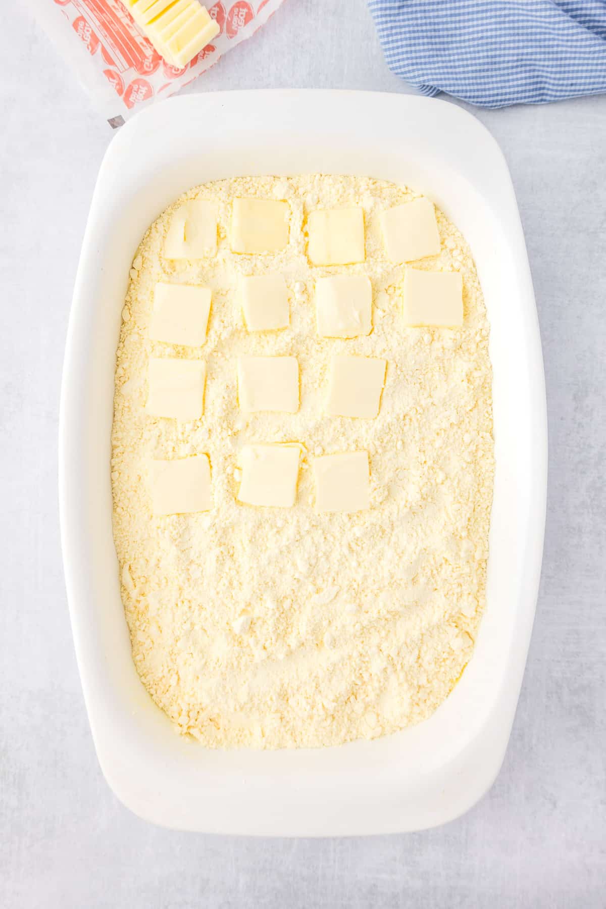 Butter squares on top of fry cake mix and other lemon dump cake layers in a pan.