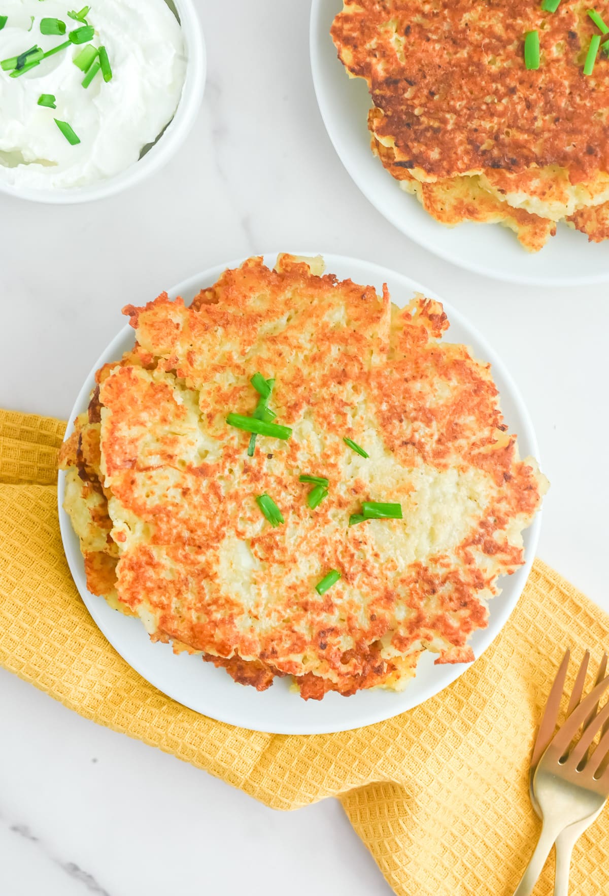 A plate of potato pancakes with sour cream and chives to the side.