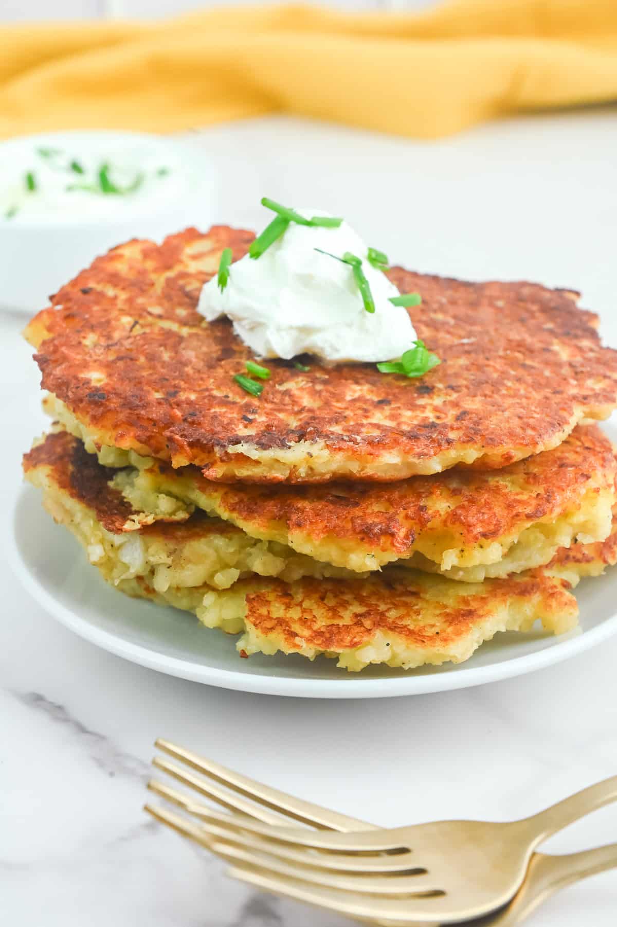 A stack of potato pancakes on a plate with sour cream and chives.