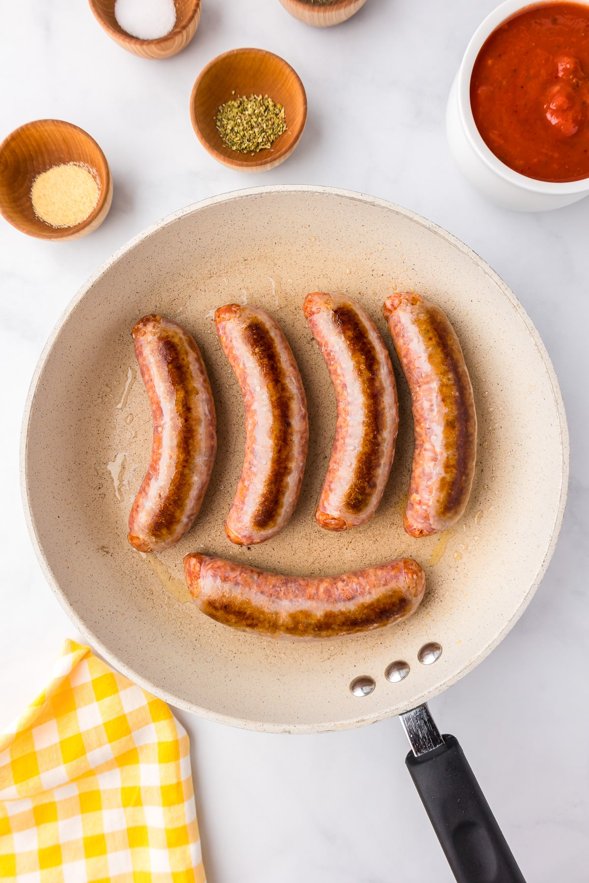 A group of Italian sausages browning in a pan.