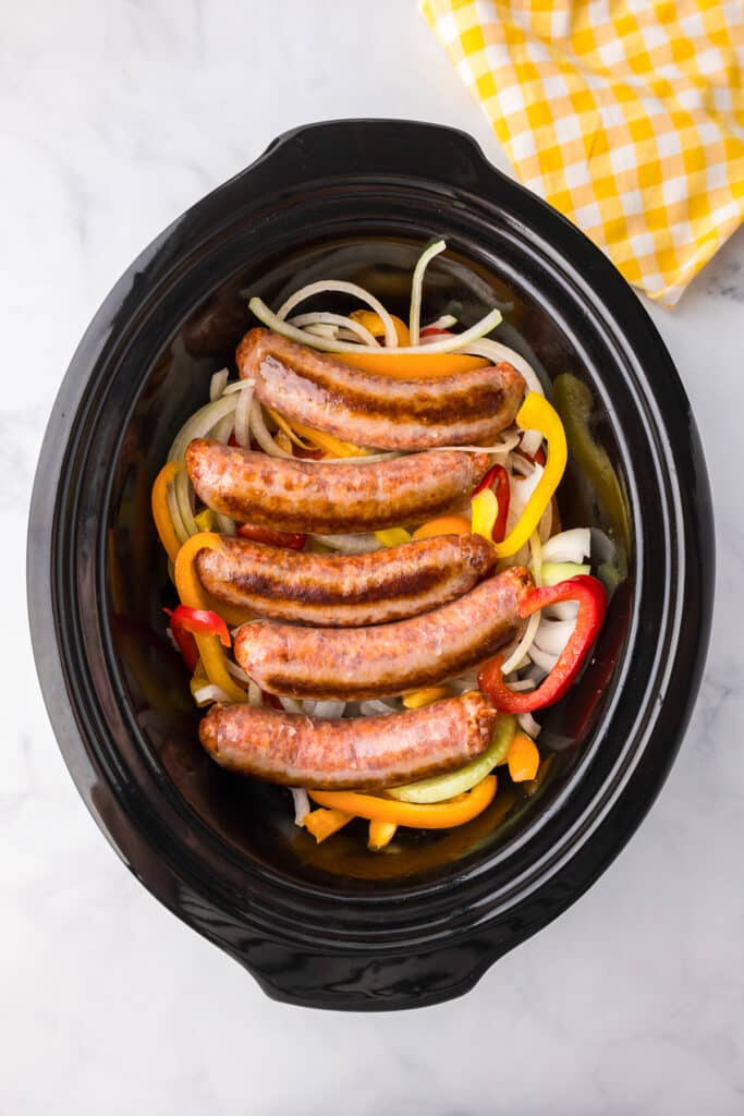 Browned Italian sausages on top of sliced peppers and onions in a slow cooker base from above.