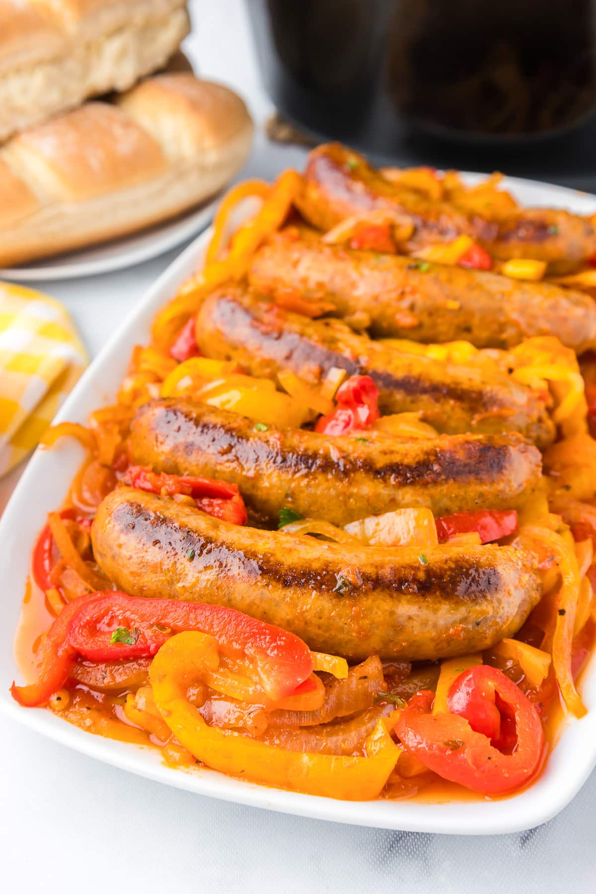 Sausages and peppers on a plate in front of a crock pot.