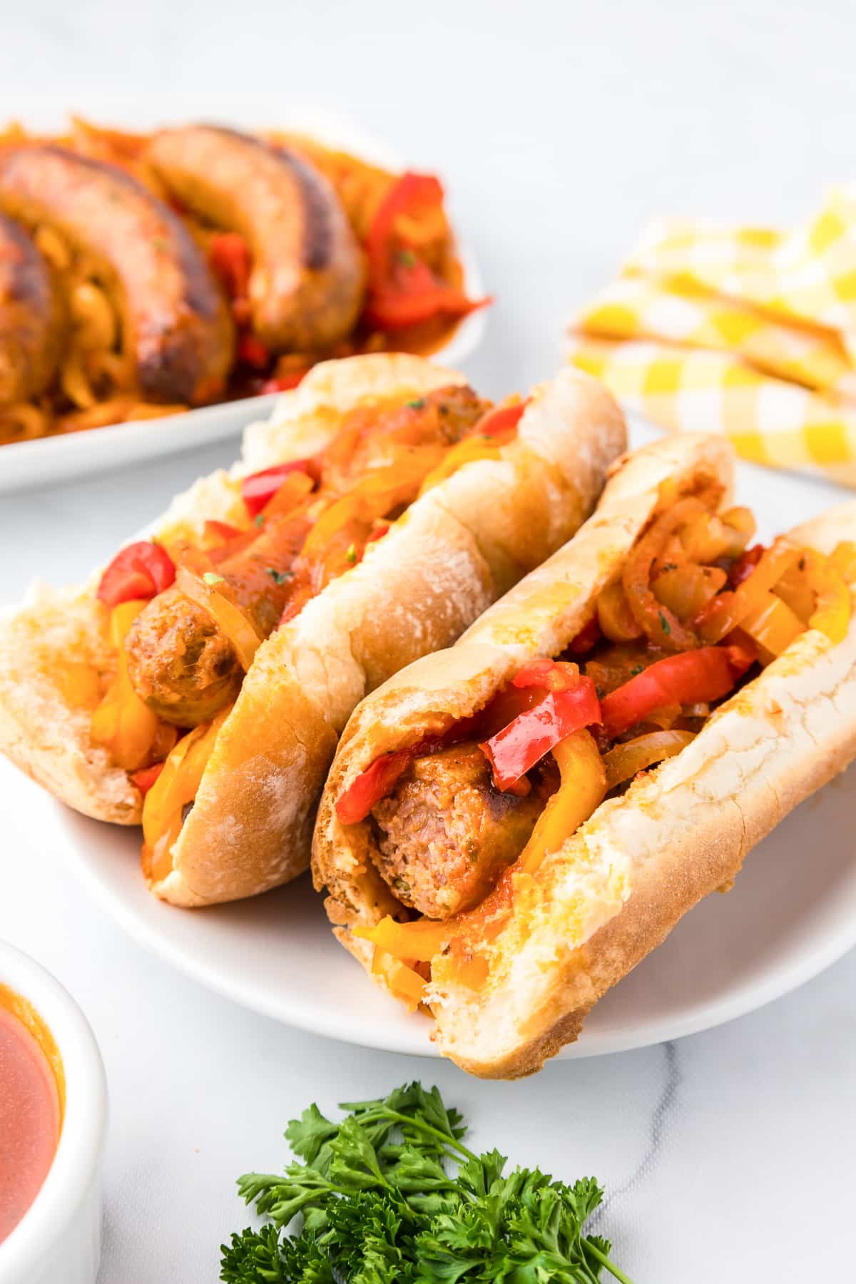 A plate with two Italian sausages on buns topped with pepper and onions with one sausage missing a bite.