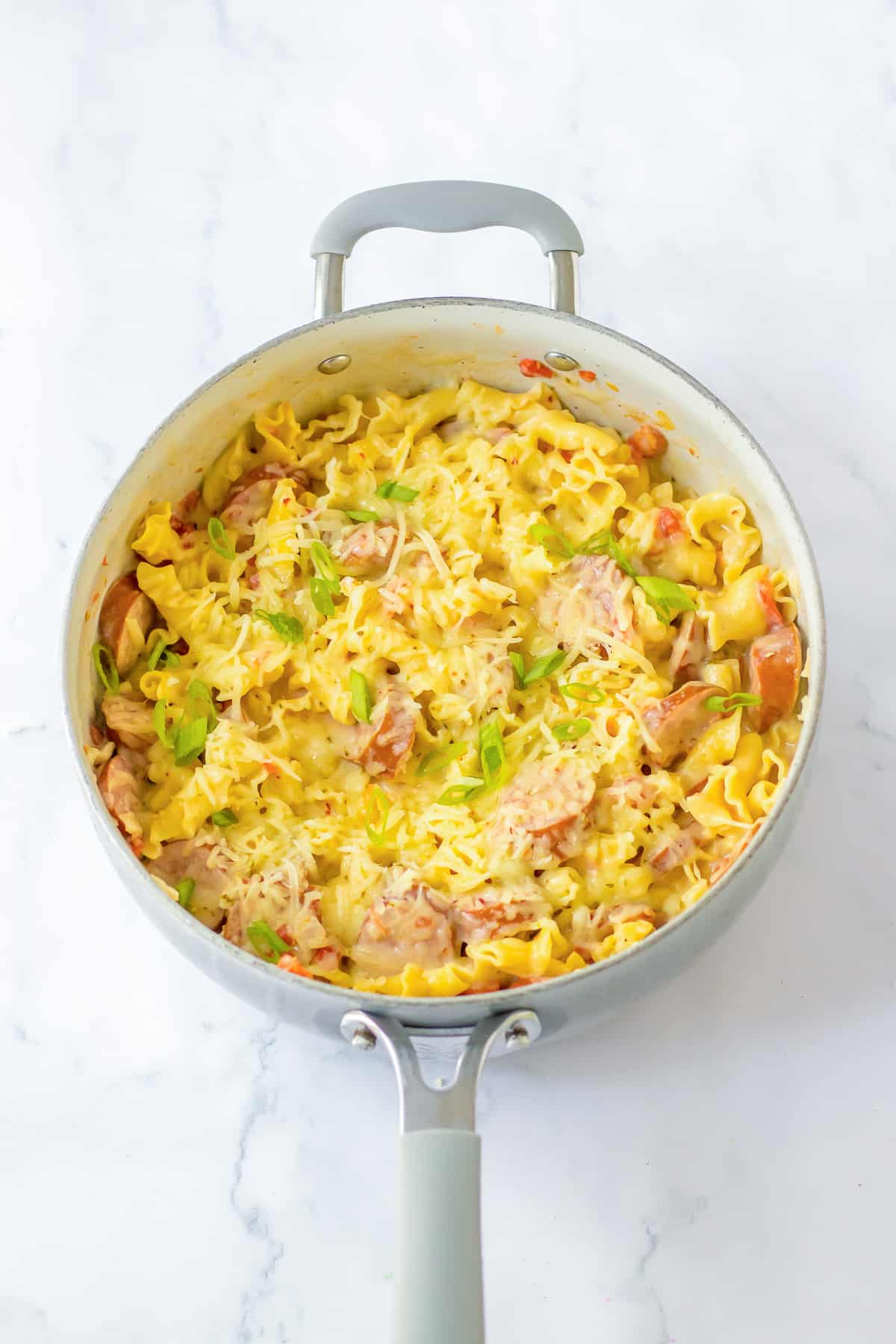 A pan full of cooked smoked sausage and pasta with melted cheese on top.