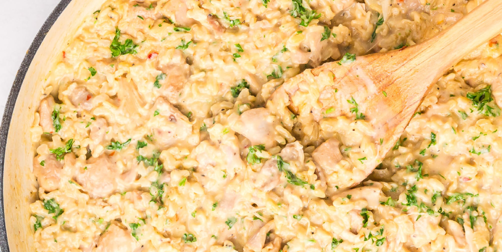 Wide view of creamy chicken and rice in the pan from overhead with a wooden spoon stirring.