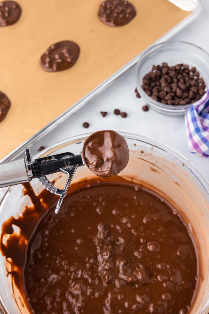 Liquidy chocolate chip flourless brownie cookie batter being scooped with a cookie scoop.