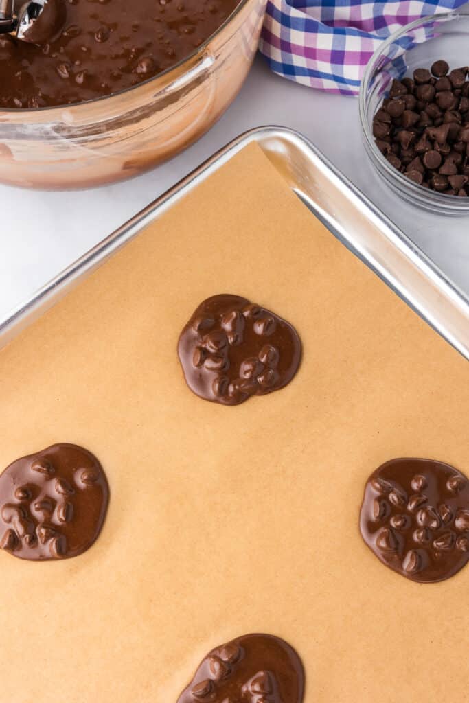 A pan lined with parchment paper with liquidy cookies on the pan.