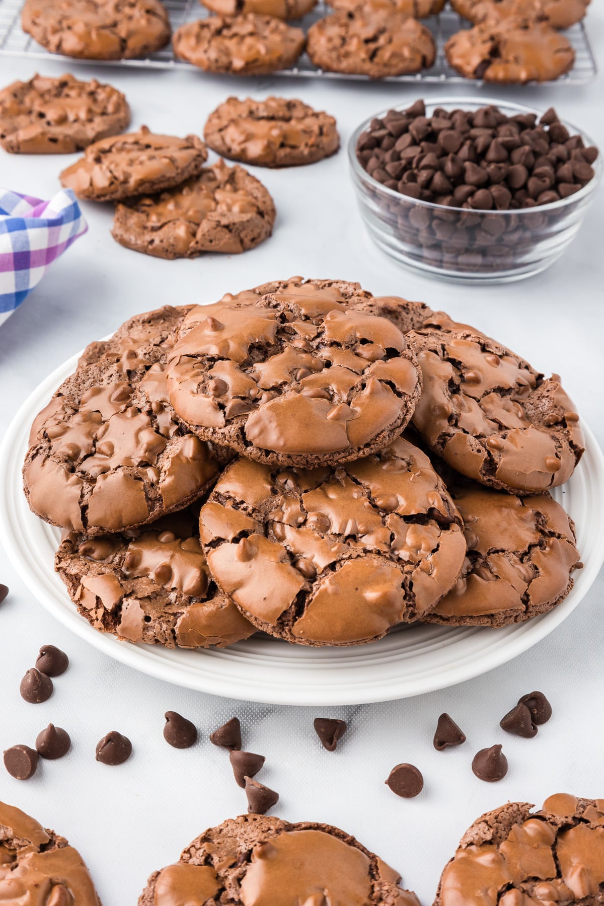 A plate of flourless chocolate brownie cookies with more cookies on a cooling rack in the background.