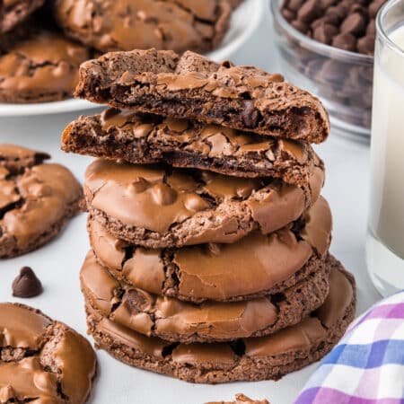 A stack of flourless chocolate brownie cookies with the top cookie broke in half to see the center next to a glass of milk.