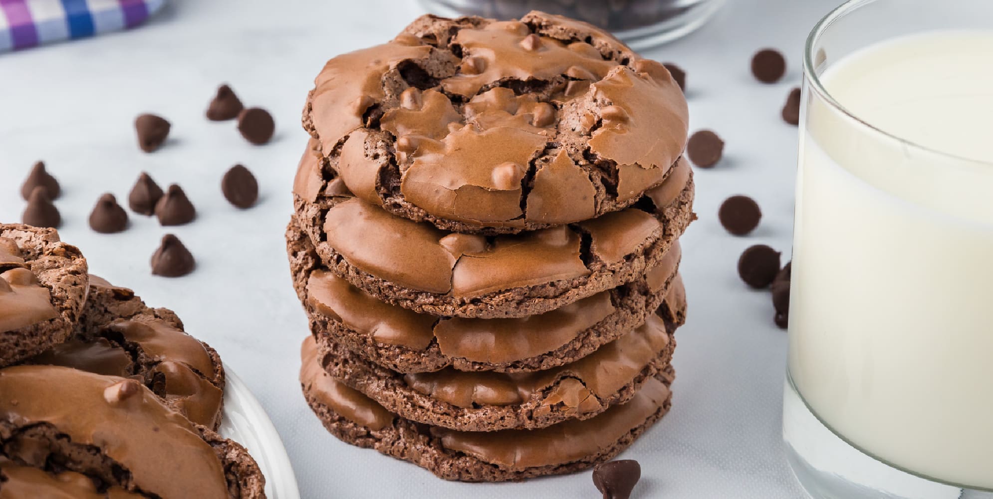 A wide video of a stack of flourless chocolate brownie cookies next to a glass of milk with more cookies on a plate nearby.