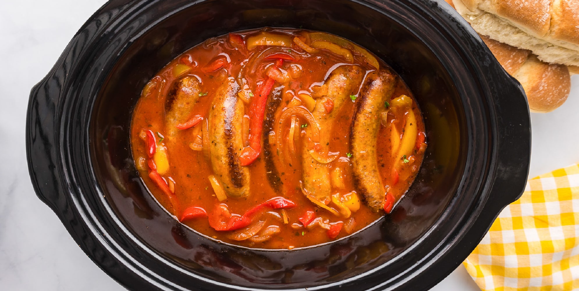 Wide view of a slow cooker full of Italian sausage, peppers and onions in a tomato sauce.