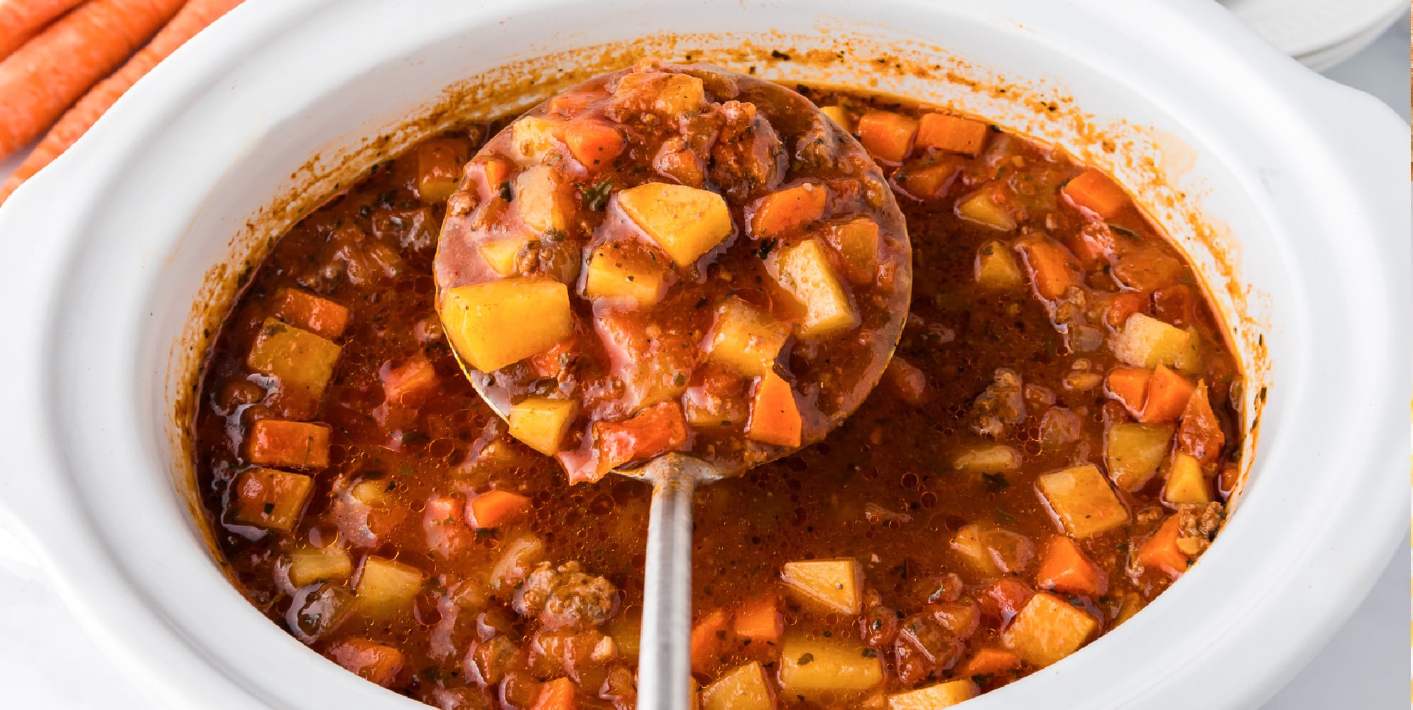 A crock pot of hamburger stew with carrots and potatoes being lifted from the side with a large ladle.