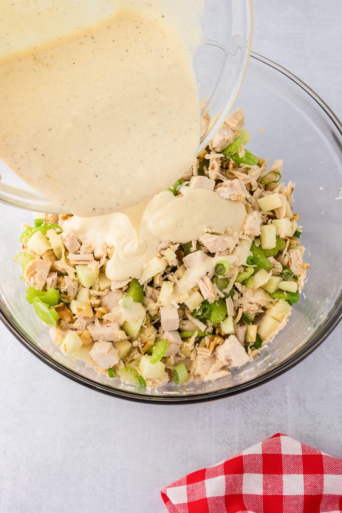 Dressing being poured into a bowl of chopped chicken, apples and celery pieces to make apple walnut chicken salad.