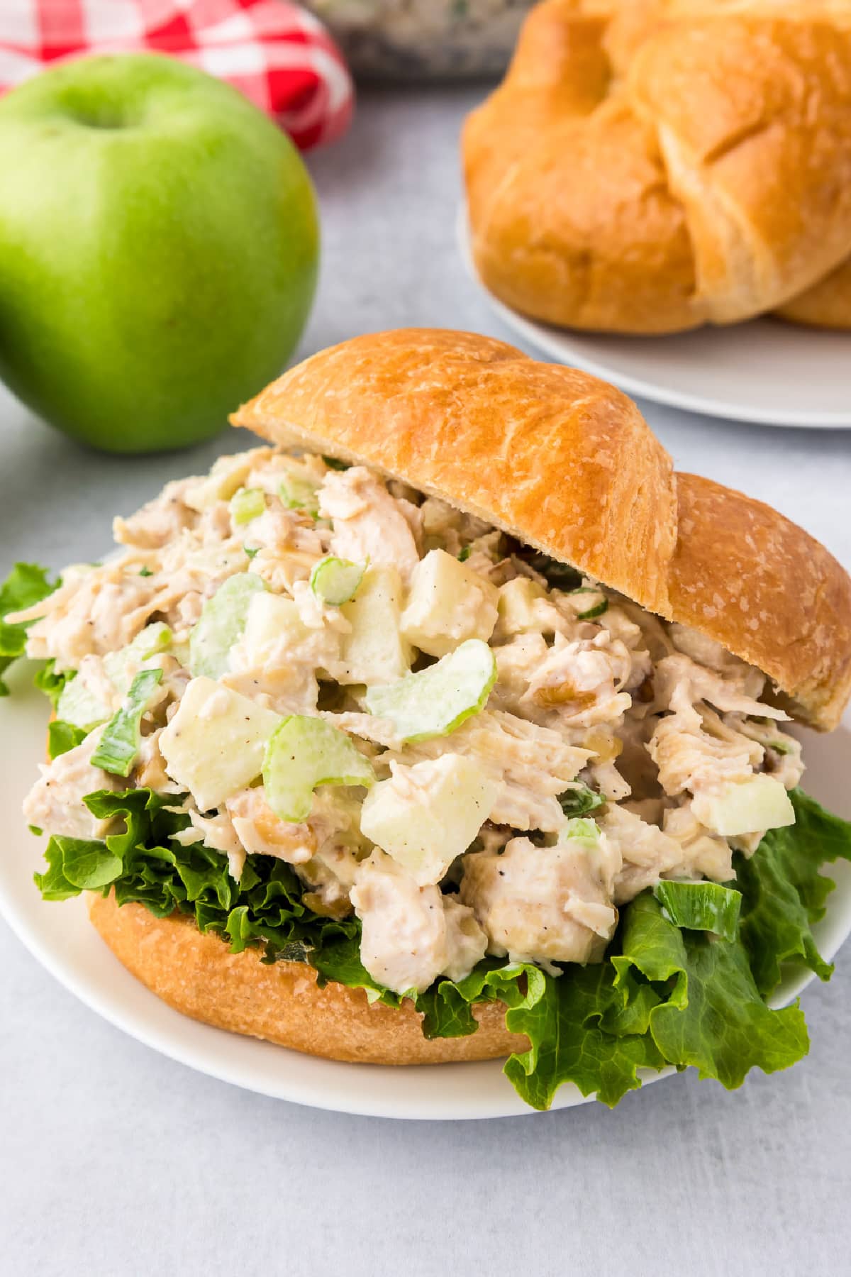 A apple walnut chicken salad sandwich on a croissant with more apples and croissants nearby.
