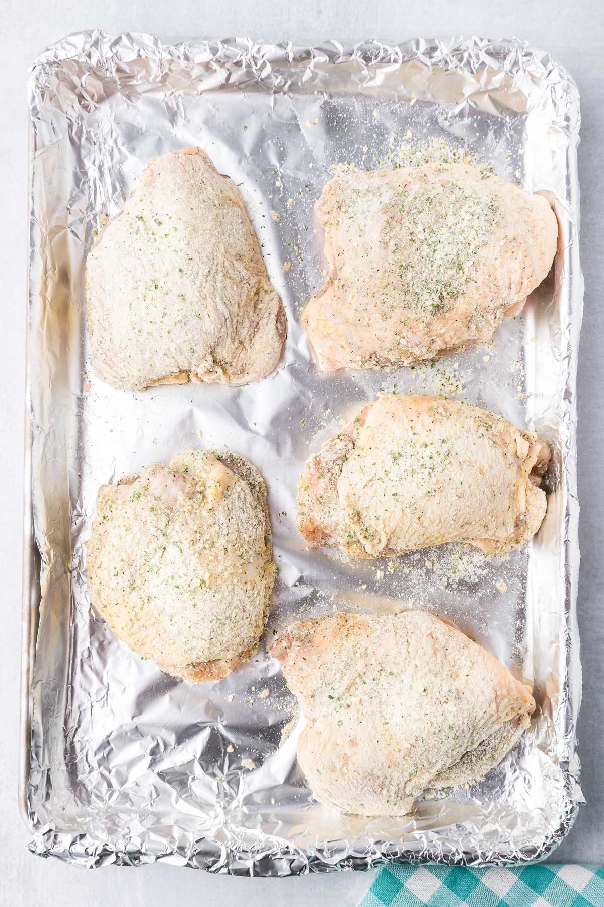 Five seasoned chicken thighs on a foil-lined baking tray, ready to be cooked.