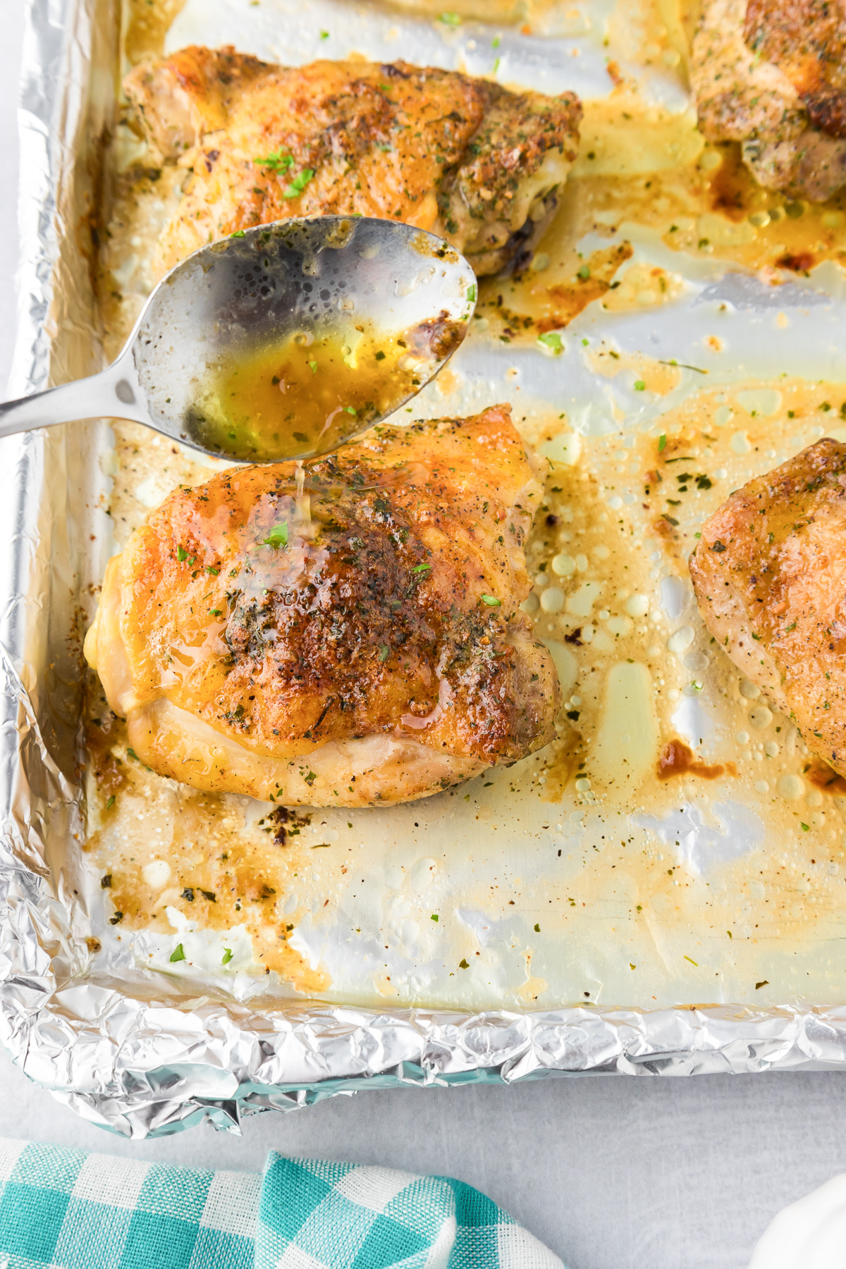 Baked crispy ranch chicken thighs on a foil-lined tray being basted with juices from the pan using a spoon.