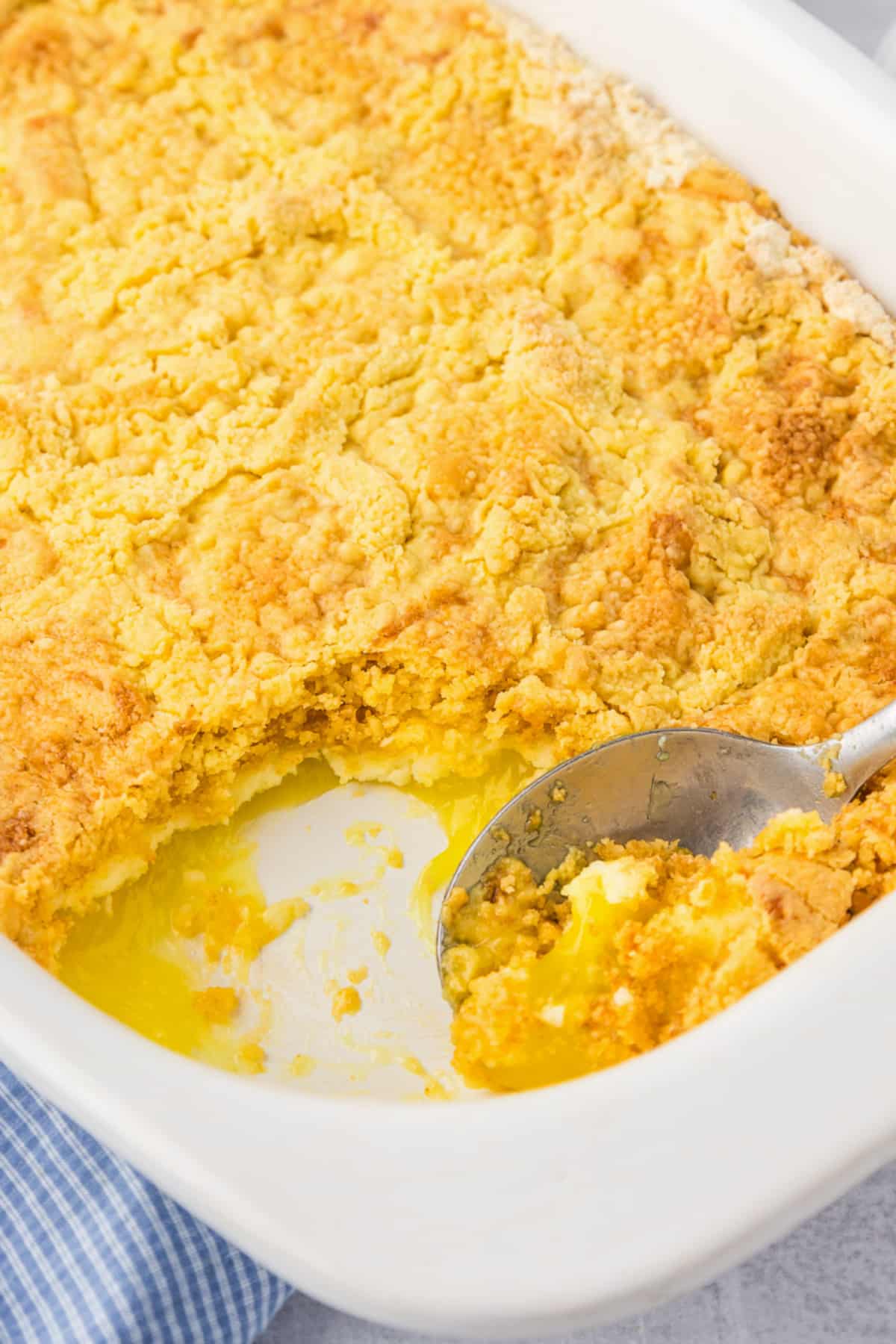 A white casserole dish full of lemon dump cake with a spoon scooping the gooey dessert.