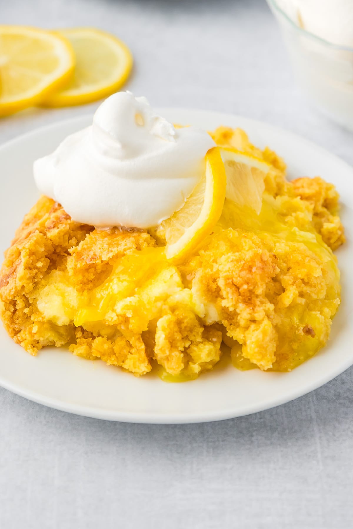 Lemon dump cake on a white plate with whipped cream and a slice of lemon on top.