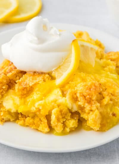 Lemon dump cake on a white plate topped with fluffy whipped cream.