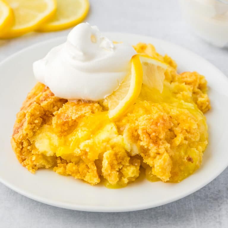 Lemon dump cake on a white plate topped with fluffy whipped cream.