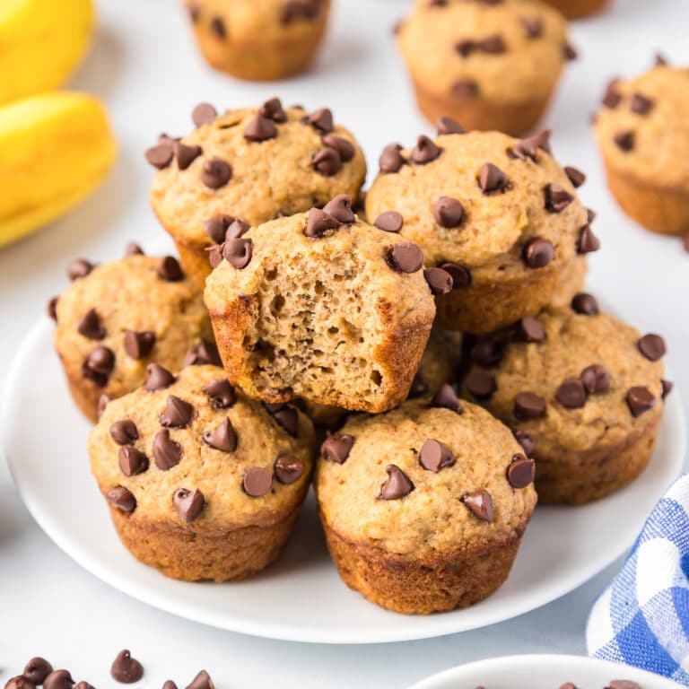 Banana chocolate chip mini muffins piled high on a plate with one muffin missing a bite.