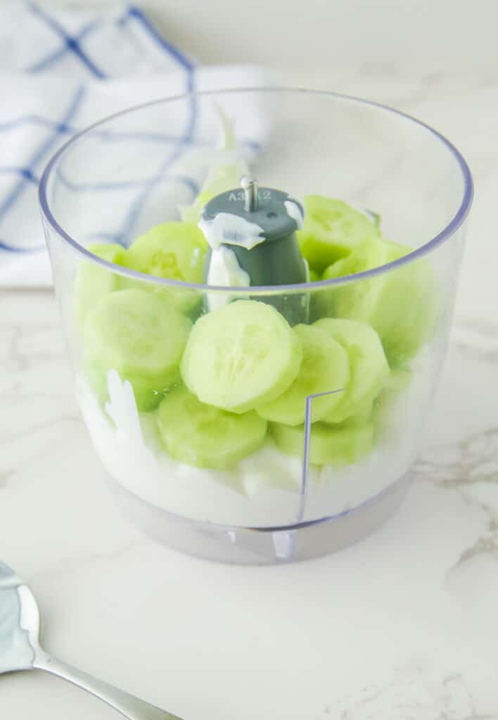 Sliced peeled cucumbers inside a food processor with yogurt ready to be blended.