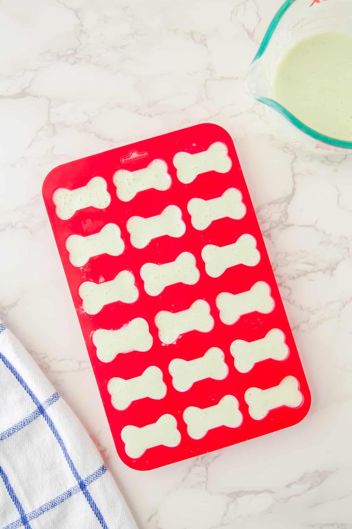 A red bone-shaped silicone mold filled with yogurt cumber mixture from above.