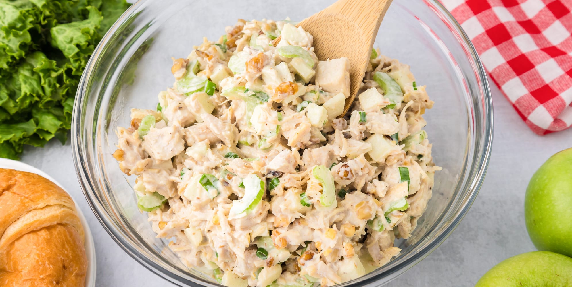 A wide view of a bowl of apple walnut chicken salad with a wooden spoon.