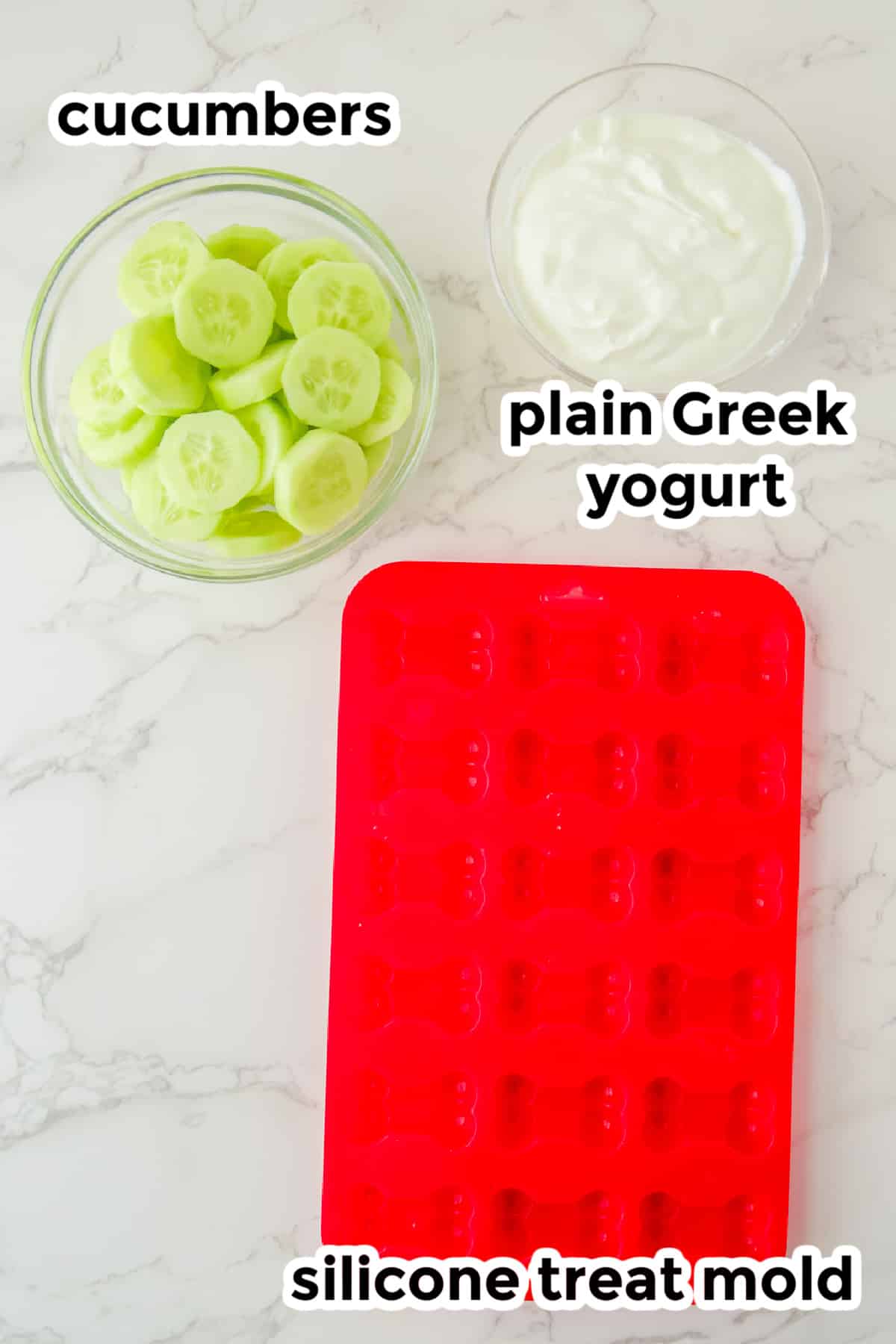 Ingredients and tools for making dog treats, including cucumbers, plain greek yogurt, and a silicone treat mold with text labels.