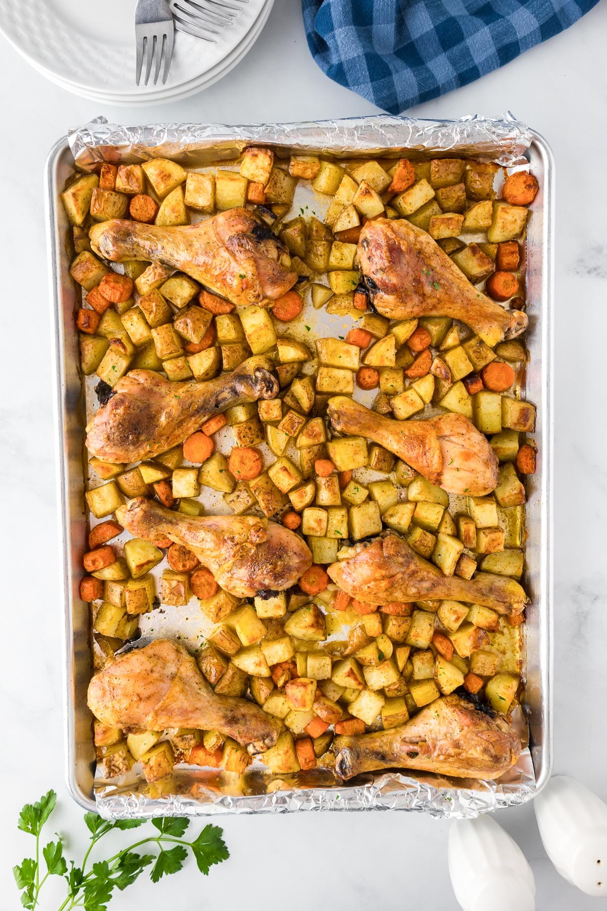 Golden brown roasted chicken legs with diced potatoes and carrots on a baking sheet.