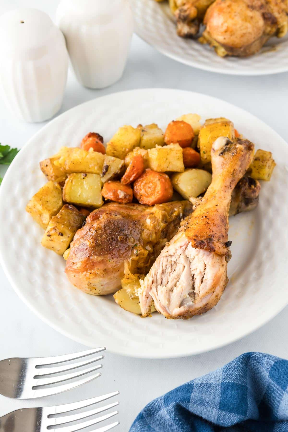 A plate with two roasted chicken legs, one missing a bite, roasted potatoes and carrots on a plate on a dinner table.