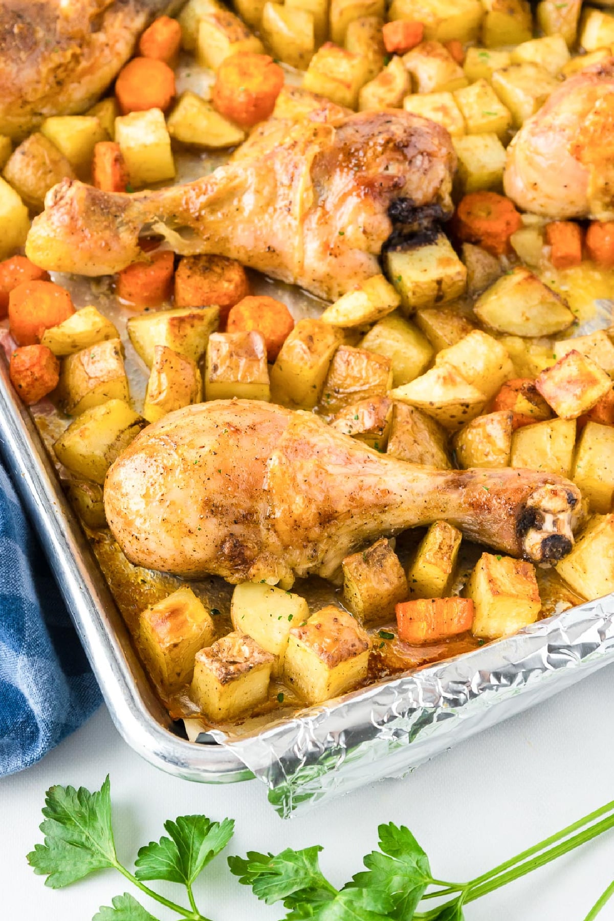 Roasted chicken legs with diced potatoes and carrots in a foil baking tray at an angle.