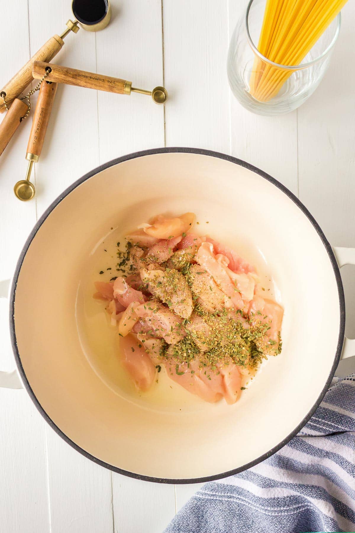 Raw chicken strips seasoned with herbs in a large pot.