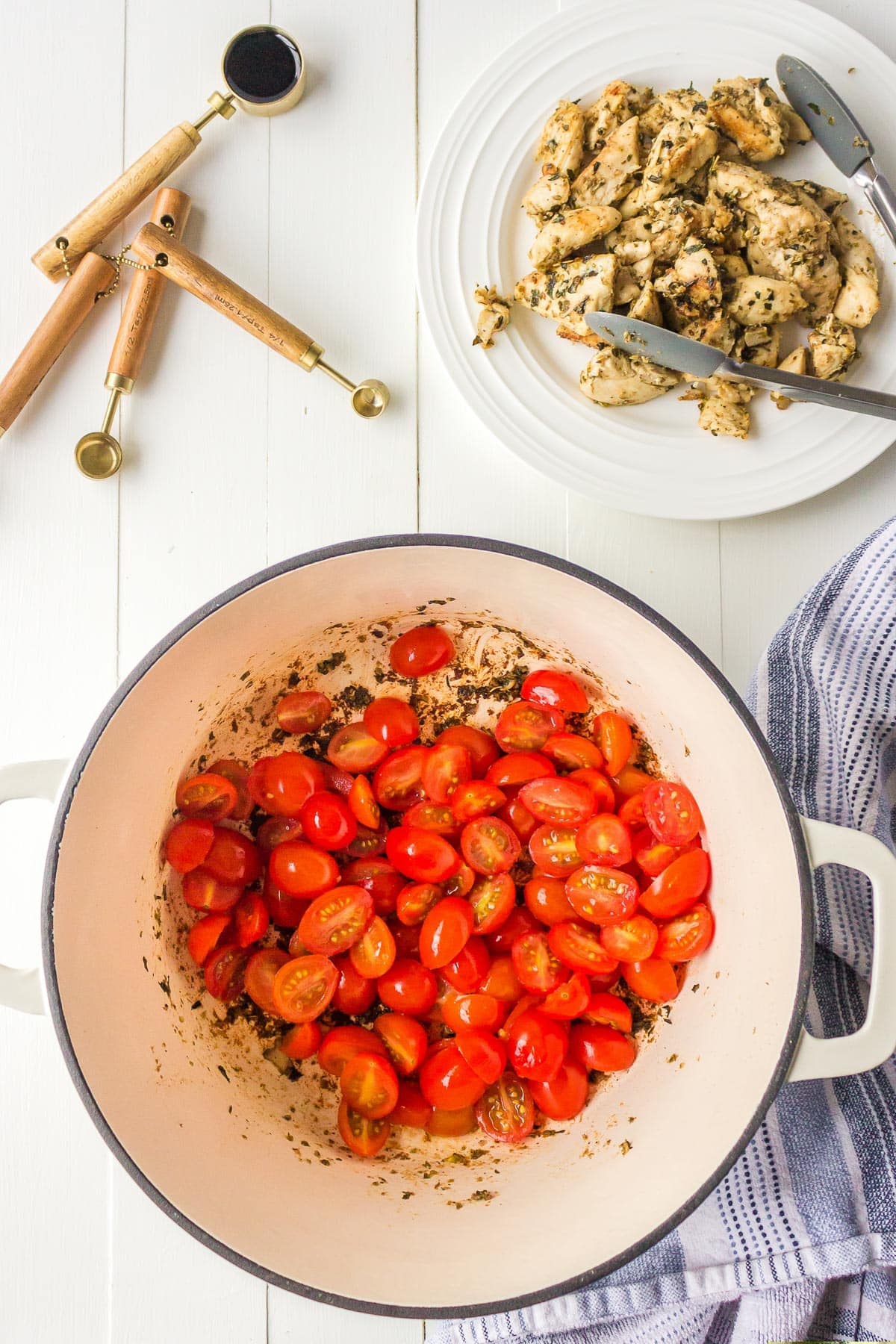 Top view of a pot with cherry tomatoes with cooked chicken and balsamic vinegar nearby.