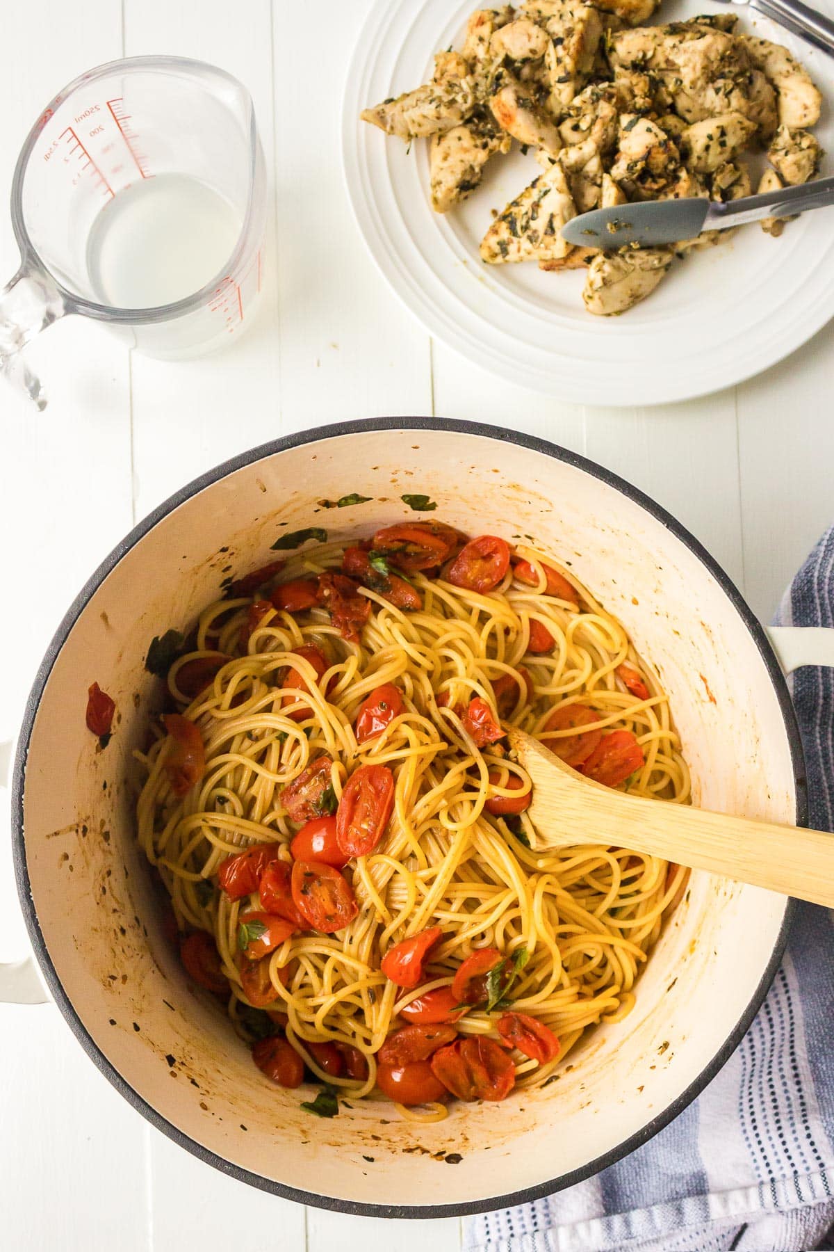 A pot of spaghetti with cherry tomatoes and herbs, with a plate of cooked chicken bruschetta nearby.