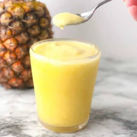 Dole whip smoothie being lifted from a glass with a spoon and a pineapple in the background.