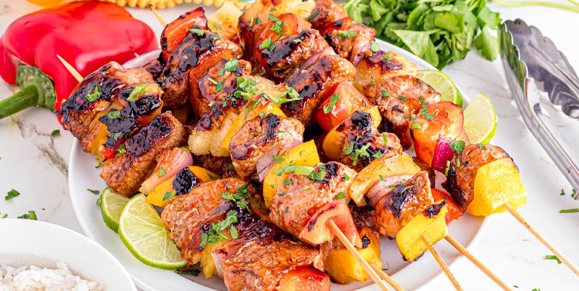 Wide view of grilled pork tenderloin and vegetable skewers garnished with herbs on a plate.