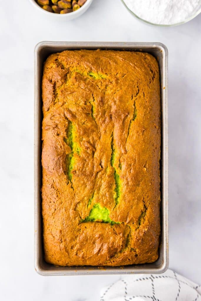 Overhead view of a freshly baked loaf of pistachio bread in a metal bread pan on a counter.