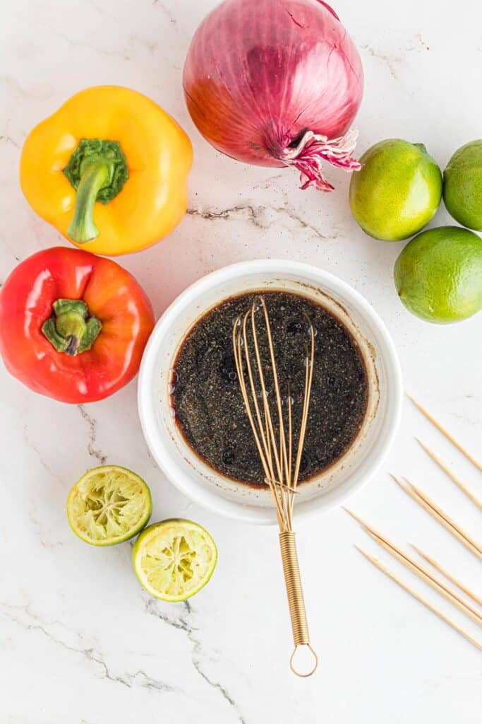 Marinade after mixing with a whisk in the bowl surrounded by fresh vegetables.