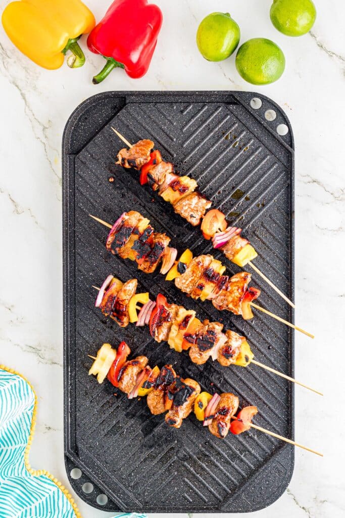 Grilled pork tenderloin skewers after cooking with bell peppers, onions, and pineapple on a grill pan.