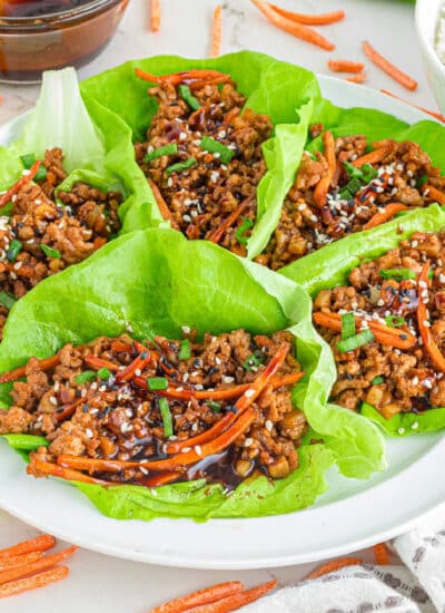 Asian-style ground pork lettuce wraps with ground meat and vegetable filling on a platter garnished with sesame seeds and served with rice on the side.