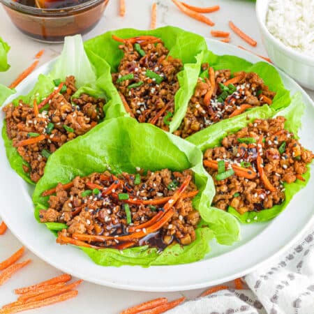 Asian-style ground pork lettuce wraps with ground meat and vegetable filling on a platter garnished with sesame seeds and served with rice on the side.