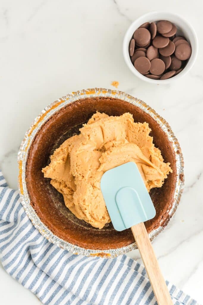 A bowl of peanut butter buckeye pie filling being spread with a silicone spatula in a chocolate pie crust.