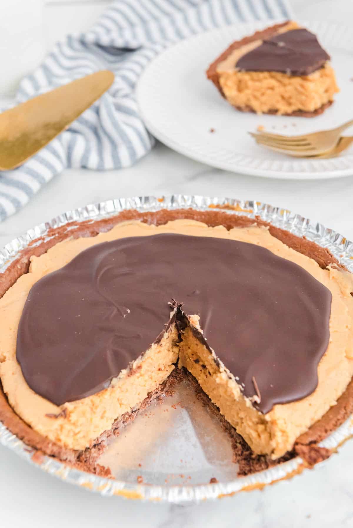 A pie with a chocolate topping and peanut butter filling, with one slice missing. A slice is served on a plate in the background.