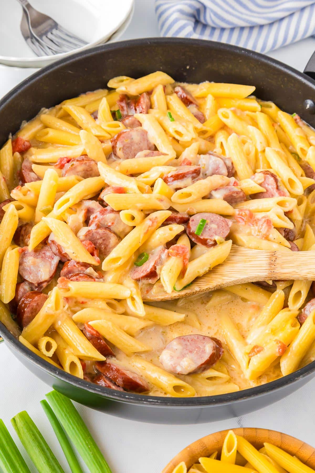 A skillet filled with creamy cheesy smoked sausage pasta being scooped by a wooden spoon.
