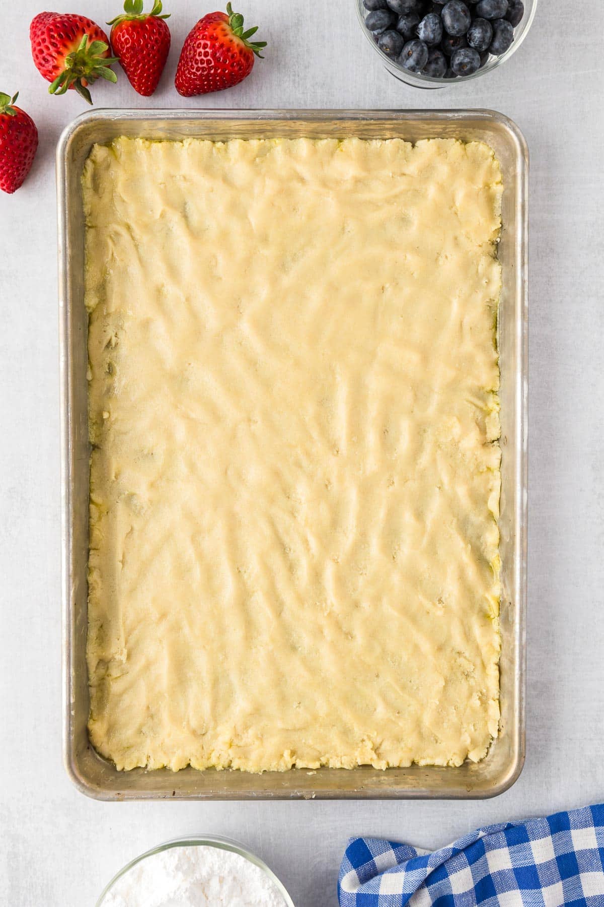 A rectangular baking tray filled with uncooked sugar cookie dough on a counter.
