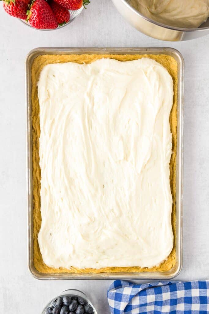 A rectangular rimmed cookie pan tray filled with sugar cookie topped with a white frosting.