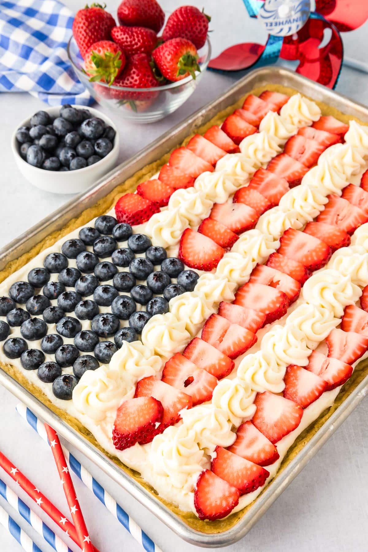 A rectangular pan of fruit pizza is decorated to resemble the American flag, with blueberries for stars and strawberries with cream for stripes.