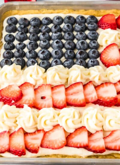 A flag fruit pizza decorated like a USA flag in a cookie pan with frosting and fruit decorations.